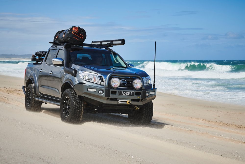image of a 4WD driving on the beach with an awning and luggage carrier installed on their roof racks
